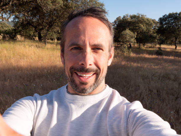 a man captures a selfie in a scenic countryside setting under a clear blue sky.